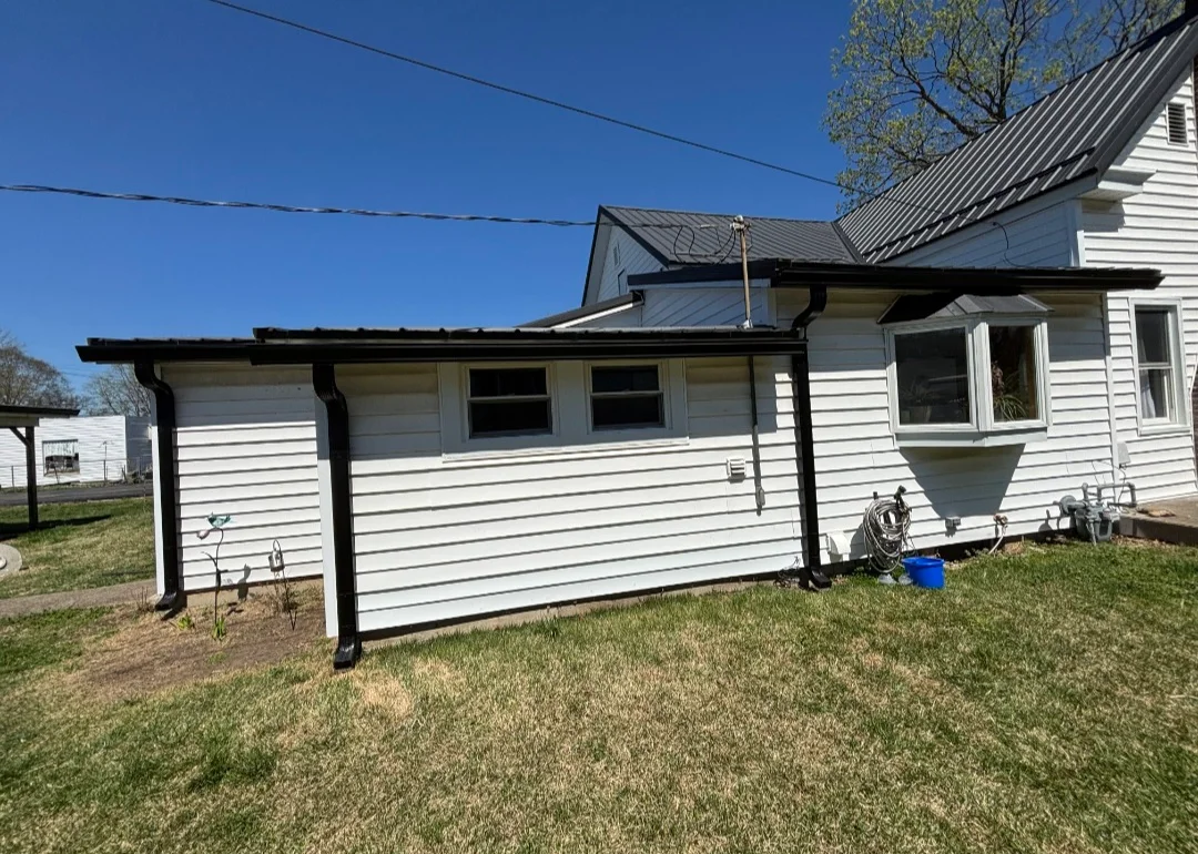 Black steel patio cover with beam framing attached to white vinyl-sided house