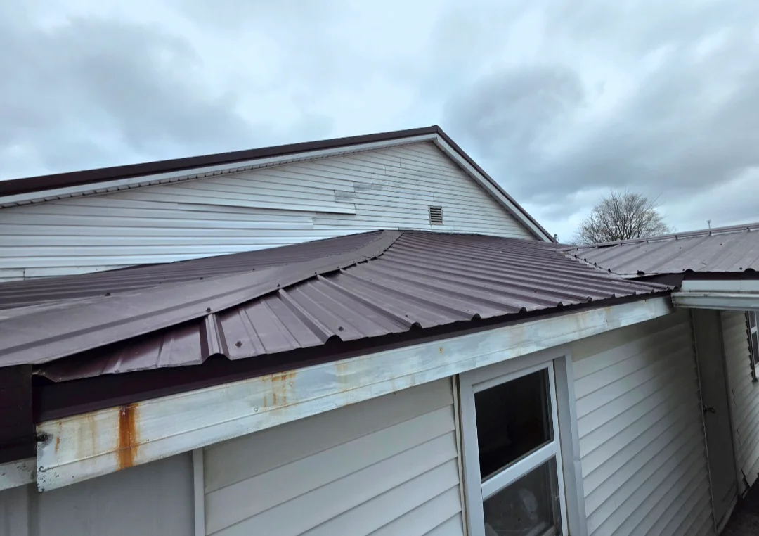 Dark metal standing seam roof installed on residential addition with white vinyl siding