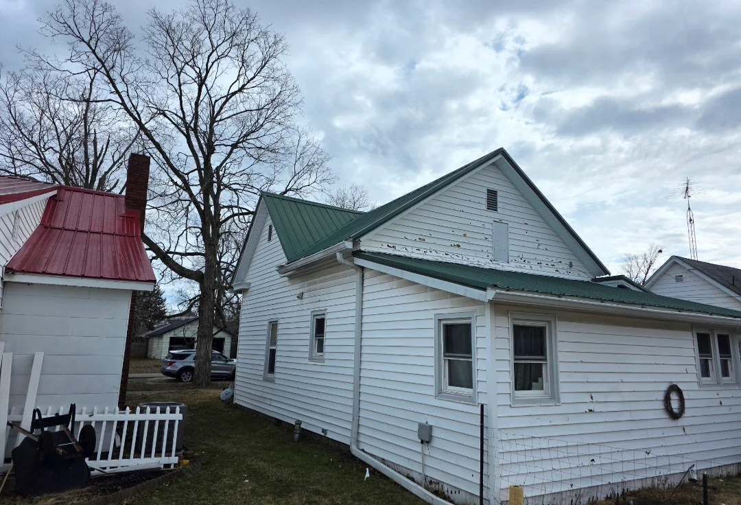 Green standing seam metal roof on white vinyl-sided house with gable design