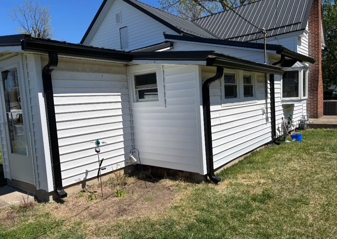Black aluminum gutters and downspouts installed on white-sided residential addition with metal roof