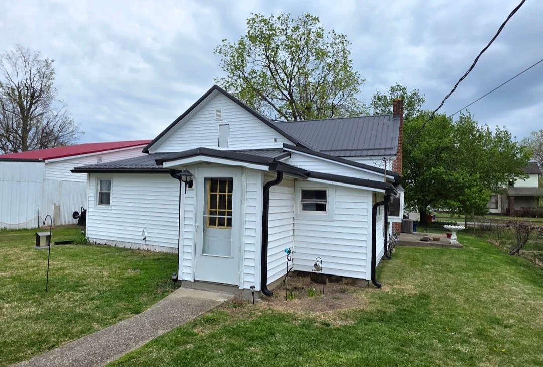 White vinyl-sided house with new dark metal roof, black trim, and updated gutters