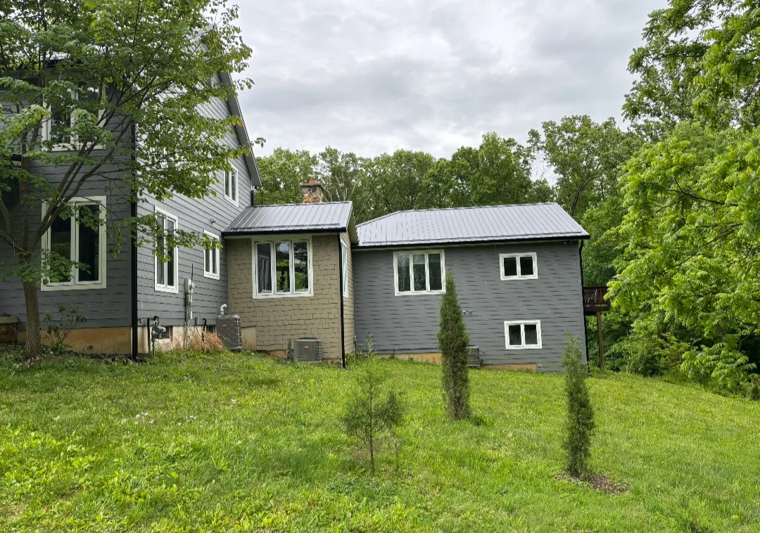 Standing seam metal roof on modern home addition with gray siding and brick chimney