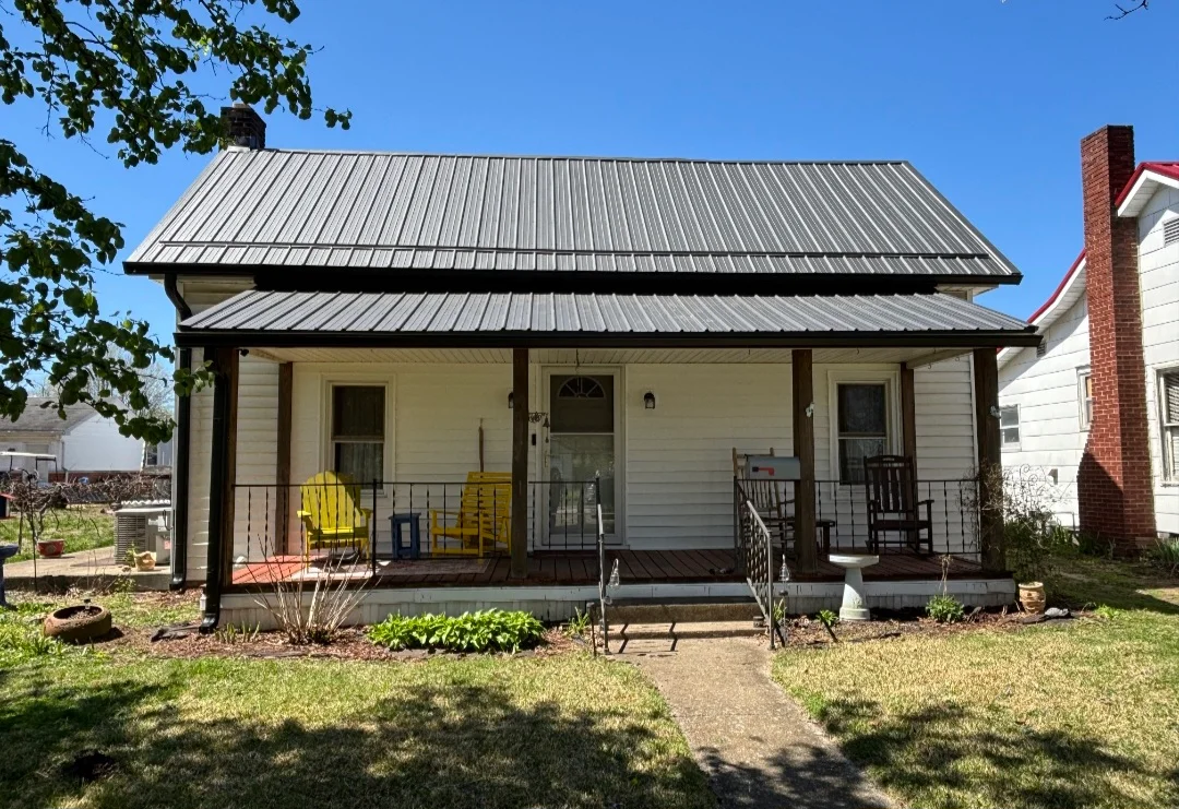 Standing seam metal roof with gray finish and timber-framed porch overhang on residential home