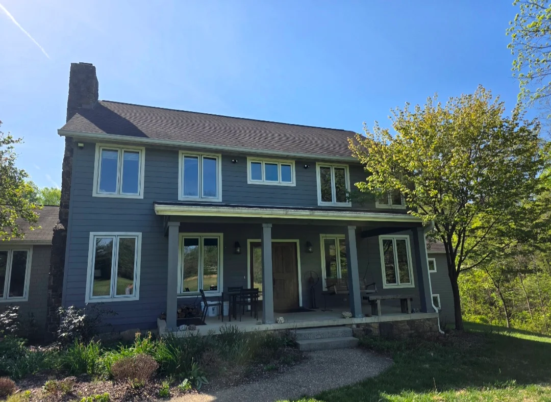 Dark blue siding colonial home with new architectural shingle roof, white trim windows, and front porch with columns