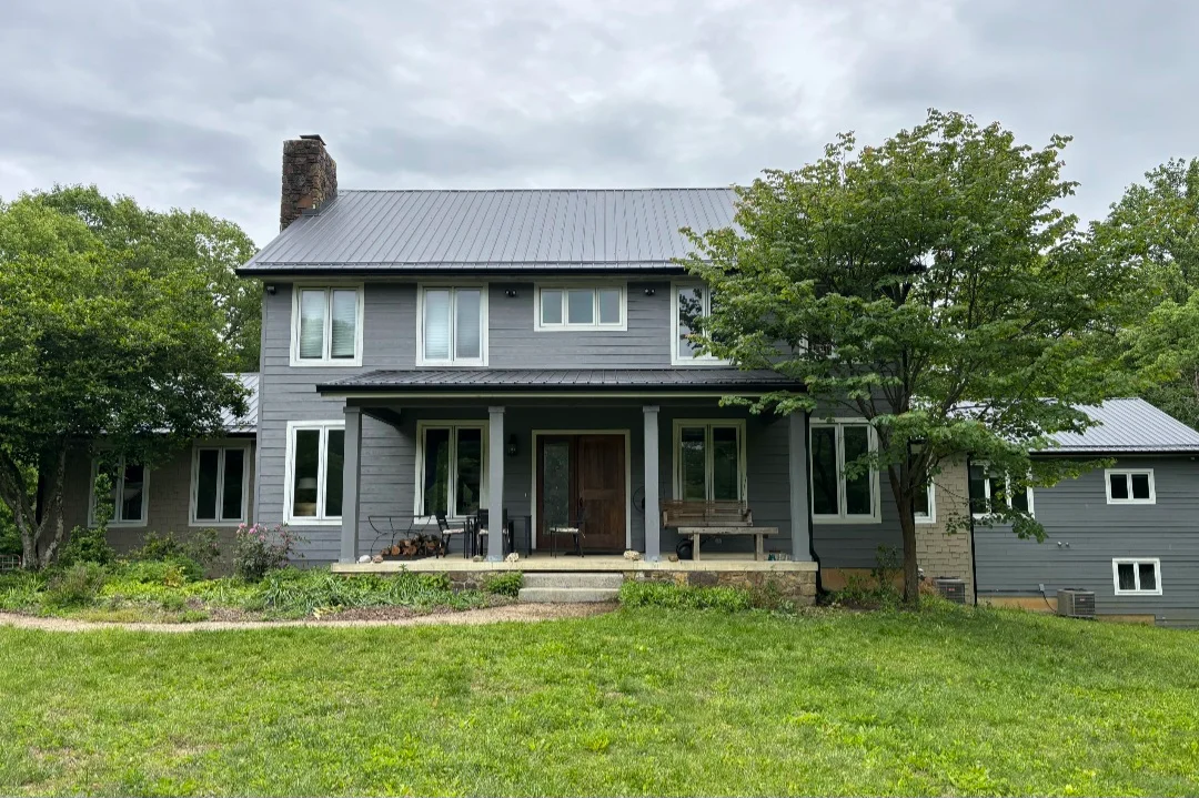 Two-story farmhouse with standing seam metal roof, gray siding, and brick chimney