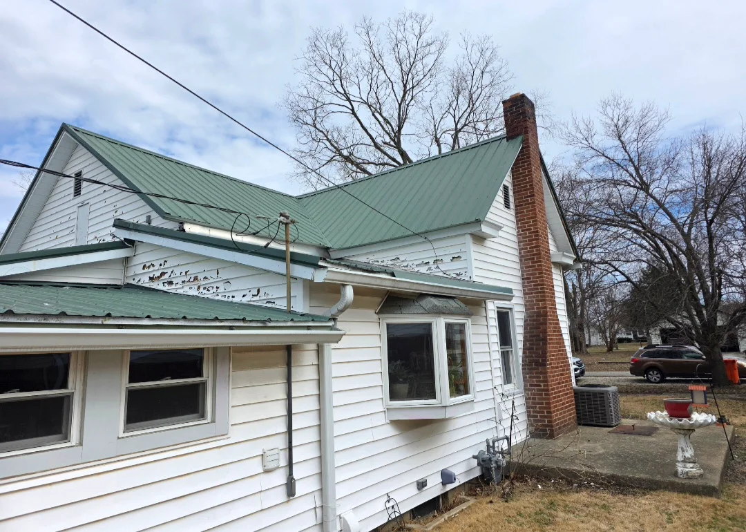 Green standing seam metal roof installed on white vinyl-sided residential home with brick chimney