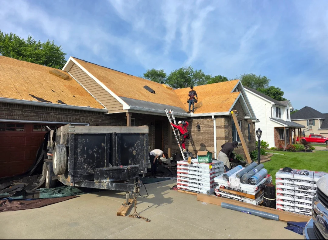 Residential roof replacement with golden tan architectural shingles, workers installing, materials staged on driveway