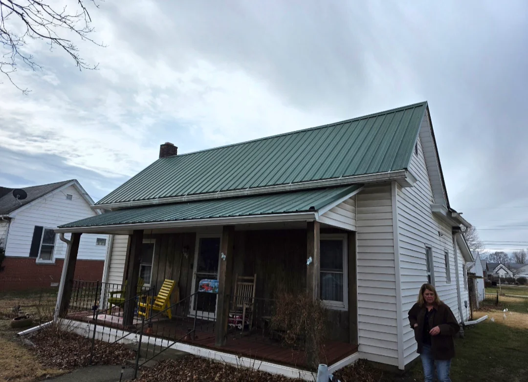 Standing seam metal roof in green with white vinyl siding and covered porch